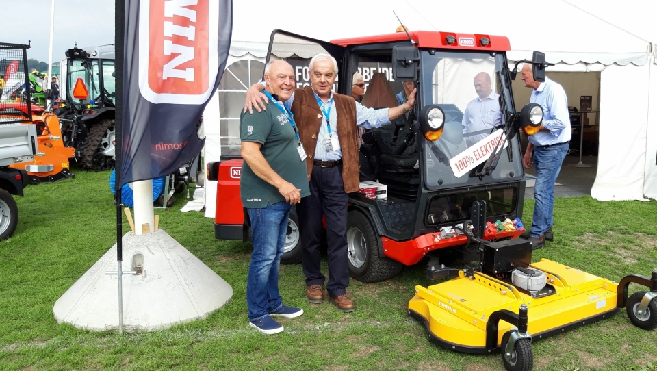 Geir Enersen (t.v.), Lier Traktor AS og Nimos-direktør Nico Drost ved den nye redskapsbæreren som ble vist på den danske utstillingen «Maskiner under broen».