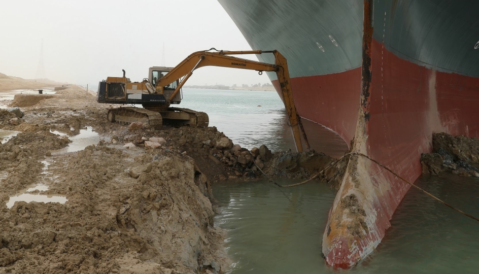 En ikke altfor stor graver er satt i arbeid for å prøve å få løs det grunnstøtte containerskipet i Suezkanalen. (Se bilde av hvor stort skipet er i forhold til graveren nedenfor).